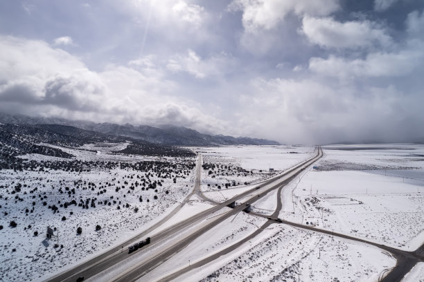 加州暴风雪后高速公路的鸟瞰图。卡车和汽车沿着山脉和沙漠在州际公路上行驶。图片下载