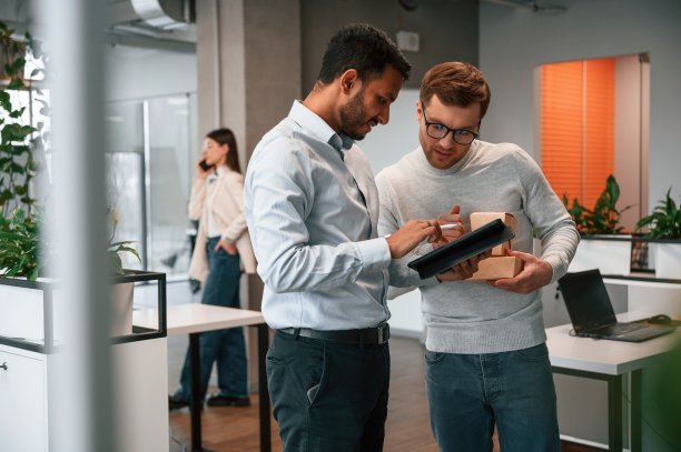 男人们拿着平板电脑和纸制环保盒。商务人士在办公室里一起工作图片下载