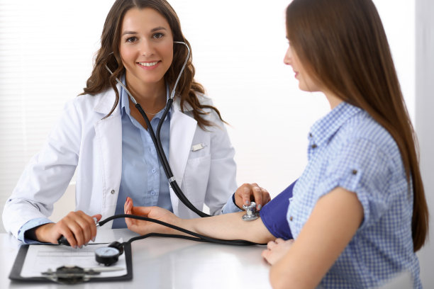 医生坐在医院办公室的桌子前检查女病人的血压。心脏病学在医学和保健方面的概念图片下载