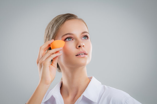 可爱美丽的自然黑发女孩清洁脸用棉花海绵微笑看着相机在白色背景。美容和水疗。图片下载