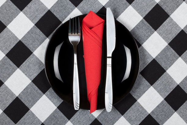 黑色的盘子，刀叉和红色的餐巾。盘子和餐具放在铺着格子布的桌子上图片下载