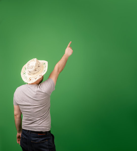 一位戴着帽子的中年农民园丁用手指着绿色背景上的一块空地。后视图。放置你的文本的地方。图片下载