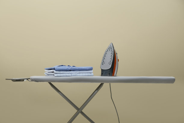 在米色的背景下，现代熨斗和干净的衣服堆叠在船上图片下载