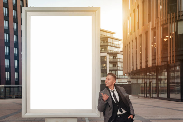 西装革履的自信青年商人指着商业大厦旁的空横幅，看着广告牌。这家伙在金融区的办公楼附近拍照。复制广告文字空间图片下载