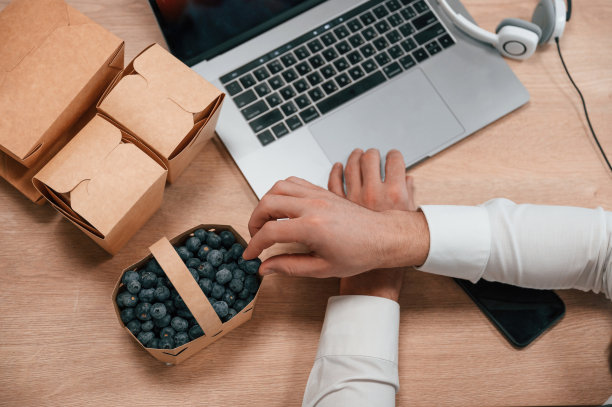 蓝莓。通过使用笔记本电脑工作的人的手的俯视图。带食物的生态盒子图片下载