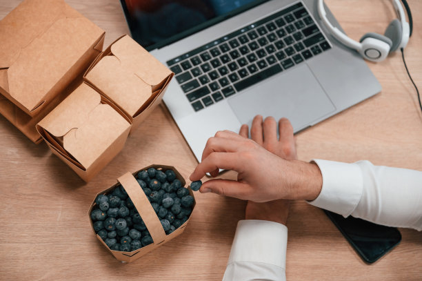 蓝莓。通过使用笔记本电脑工作的人的手的俯视图。带食物的生态盒子图片下载