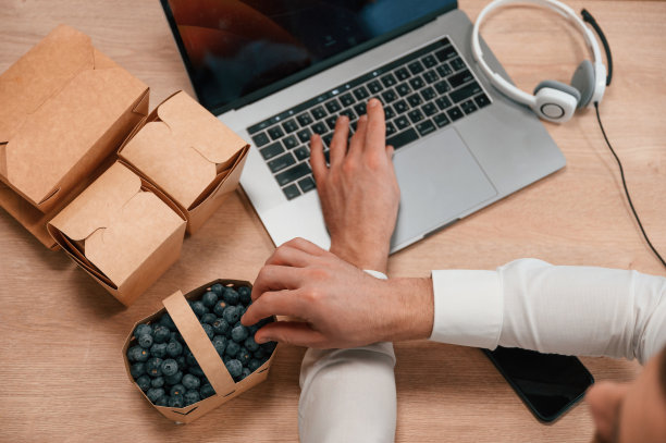 蓝莓。通过使用笔记本电脑工作的人的手的俯视图。带食物的生态盒子图片下载