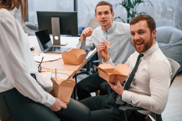 拿着饭和叉子的女人。一群同事一起在办公室吃环保盒里的食物图片下载