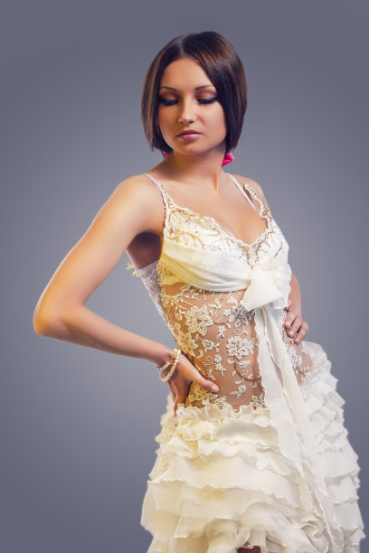 华丽性感的高加索华丽女性摆姿势在白色定制婚纱定做。针对灰色。图片下载