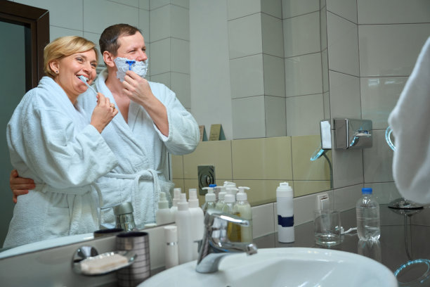 微笑的女人刷牙，而男人在浴室刮胡子图片下载
