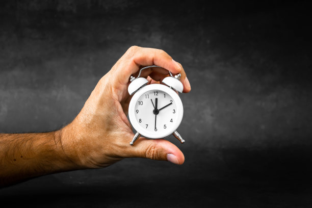 深黑背景上一个棕色人手里的红色闹钟。提及个人护理时间表，提醒风湿病、关节病和迷路炎的药物和体育锻炼。图片下载