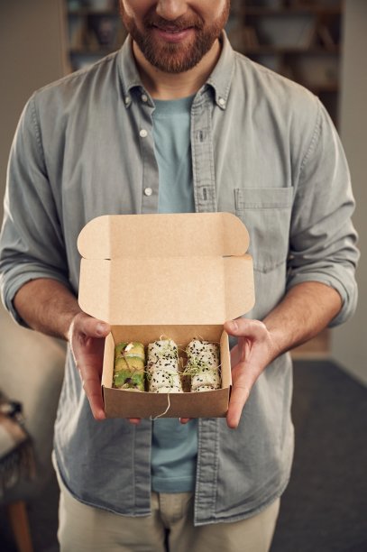 一名便装男子正拿着装在环保纸盒里的寿司图片下载