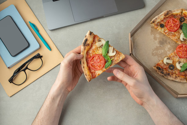 一个男人一边工作一边吃披萨，俯视图，双手放在桌面上。披萨外卖。图片下载