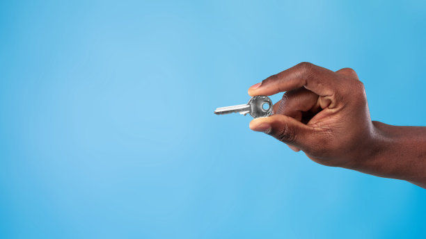 无法辨认的年轻黑人男子在蓝色工作室背景上持有金属房子钥匙，横幅设计与复制空间图片下载