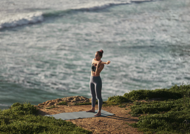 年轻的光脚女子伸展手臂在瑜伽课附近的海洋图片下载