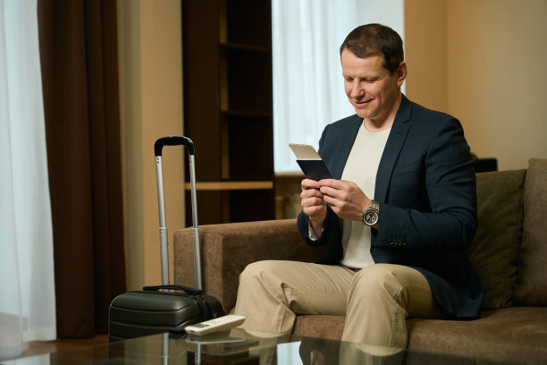 一名男子带着旅行箱坐在酒店房间的安乐椅上图片下载