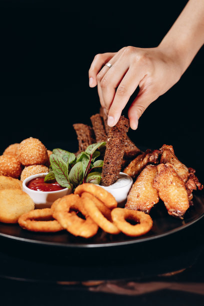 啤酒。油炸黑面包，芝士球，洋葱圈，和炸熟的鸡翅。装在黑色盘子里，配上两种酱汁。图片下载