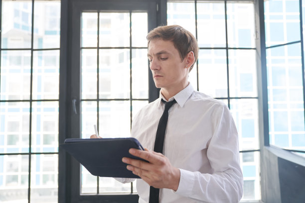 一个年轻的商人在办公室里工作，背景是一扇窗户。他使用带有触摸屏的平板电脑，在上面阅读电子邮件。有空间复制。高质量照片图片下载