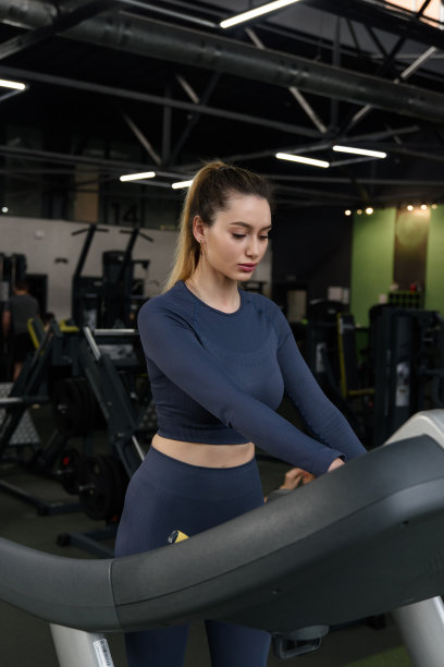 在跑步机上的美丽肌肉女人的肖像。穿着蓝色紧身裤和长袖上衣图片下载