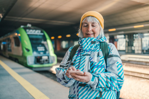 60年代快乐的女游客穿着运动服，拿着火车票站在火车站用智能手机图片下载