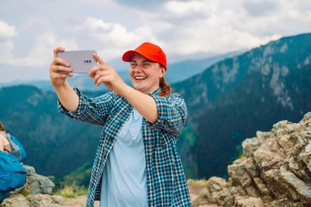 游客在山顶用智能手机拍照。戴着帽子背着背包的白人女性。旅行的概念。图片下载