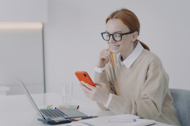 微笑的年轻女子在工作场所或课堂上发短信。女孩在办公室工作时分心了。图片下载