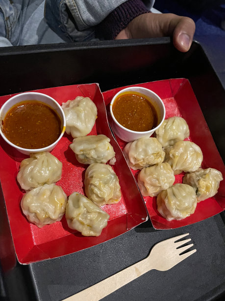 图片上是两盘蒸熟的Momos(南亚饺子)，白面粉和水面团，馅料是猪肉和混合蔬菜，放在红色纸板盘子上，作为蘸酱的电影院小吃图片下载