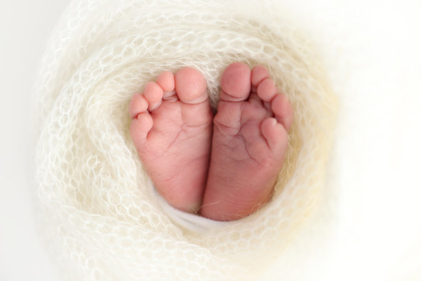 新生儿的小脚。新生儿柔软的脚躺在白色毛毯里。近距离的脚趾，脚跟和新生儿的脚。工作室微距摄影。女人的幸福。图片下载
