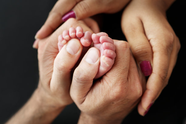 新生儿的小脚在父母的手中。爸爸妈妈充满爱的手掌。父亲的概念形象。特写，选择性聚焦。专业摄影，黑色背景图片下载
