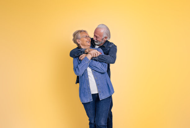 爱的深情的老夫妇手牵着手拥抱，而看着对方浪漫地在孤立的黄色背景图片下载