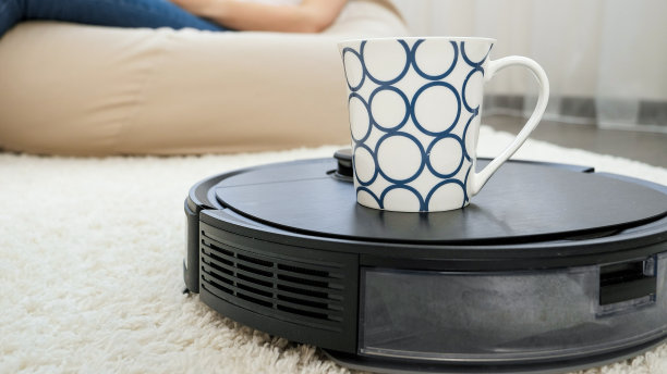 机器人吸尘器给在家办公的年轻女性送咖啡的特写镜头。现代生活中的卫生、家用电器和机器人概念。图片下载