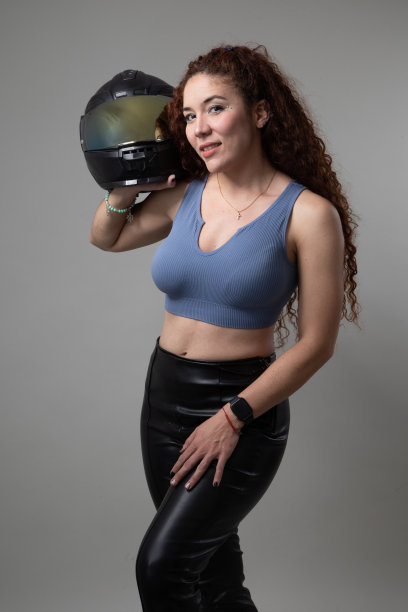 女人拿着摩托车头盔，她有长卷发，安全设备在工作室，生活方式图片下载