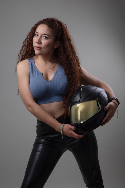 年轻的拉丁女子手持摩托车头盔，她有长卷发，安全设备在工作室图片下载