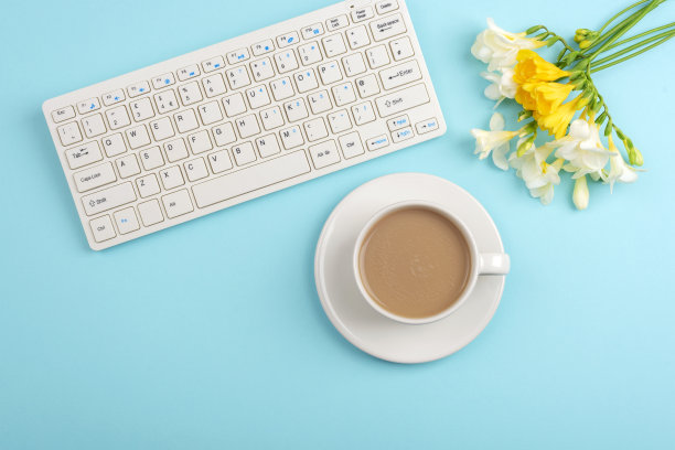 电脑键盘和咖啡杯放在有小苍兰花的蓝绿色桌子上。俯视图，平面布局，复制空间图片下载
