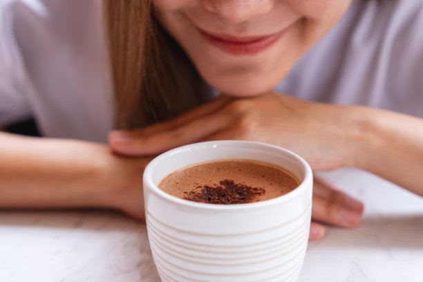 一个美丽的女人看着和闻着一杯热巧克力的特写图像图片下载