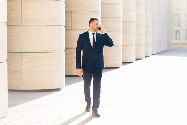 办公室男职员通过现代手机打电话，穿着正装，开心地看着一边，在户外散步，专注于一边的事情，讨论一些商业合同的细节图片下载