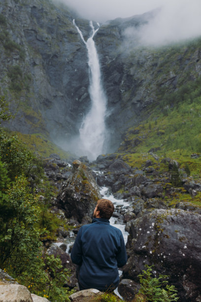 一个男人旅行者考虑在挪威瀑布风景山谷的后视图图片下载