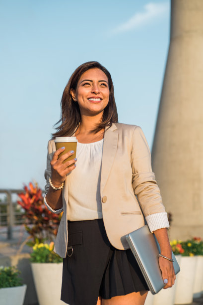 一个拉丁裔女商人手里拿着咖啡和电脑，快乐地展望未来。图片下载