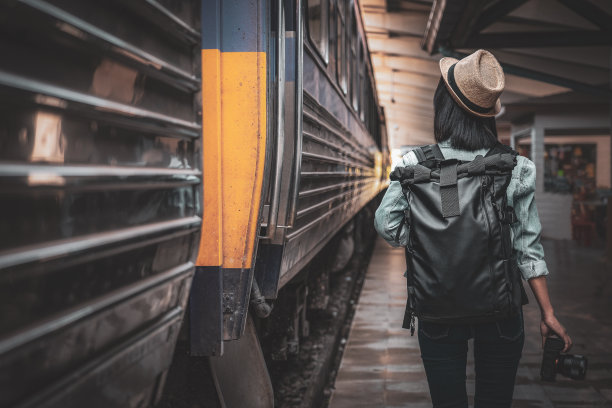 年轻的亚洲女子旅行者与背包在铁路上，背包和帽子在火车站与旅行者，旅行的概念。女游客走在火车站图片下载