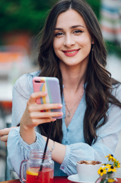 一个美丽的女人坐在街头咖啡馆和使用智能手机的肖像图片下载