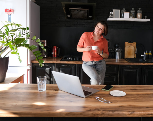 妇女工作与笔记本电脑在家里在厨房背景。自由职业者在家办公的概念。图片下载