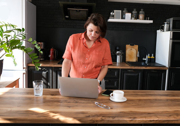 妇女工作与笔记本电脑在家里在厨房背景。自由职业者在家办公的概念。图片下载