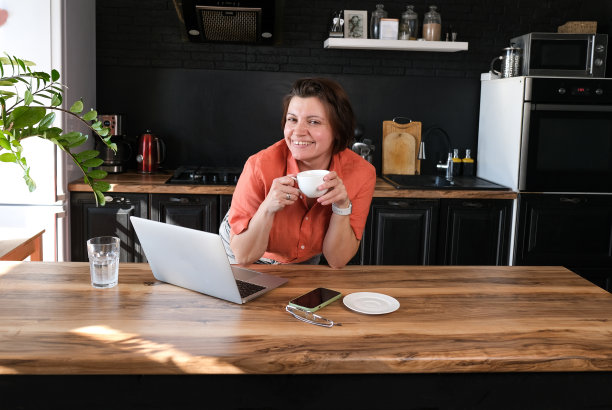 妇女工作与笔记本电脑在家里在厨房背景。自由职业者在家办公的概念。图片下载