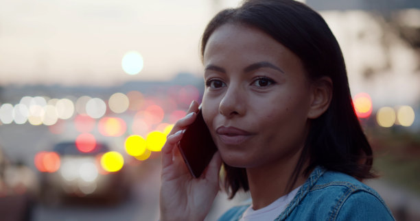 一名非裔美国妇女在城市的夜晚打电话，背景是灯光图片下载