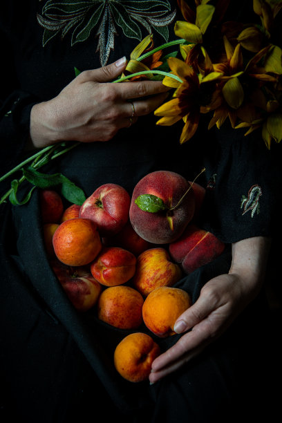 围裙里夹着新鲜桃子和杏子的女人。图片下载