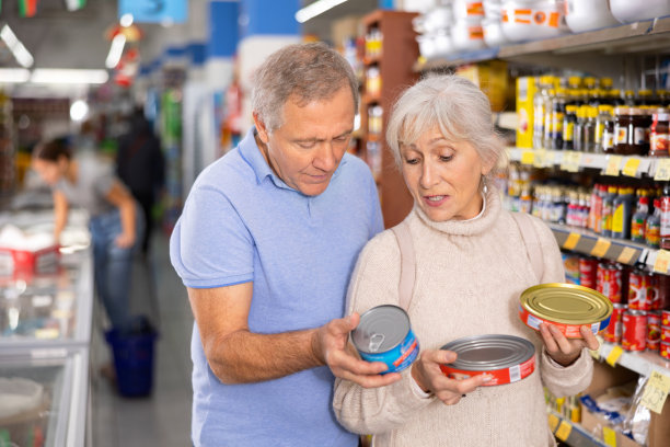 男女采购员在大超市挑选鱼罐头图片下载