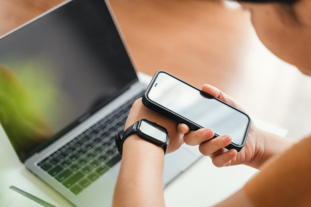 女性使用智能手机和智能手表跟踪家里客厅沙发上的活动，手表和手机之间的无线连接。图片下载