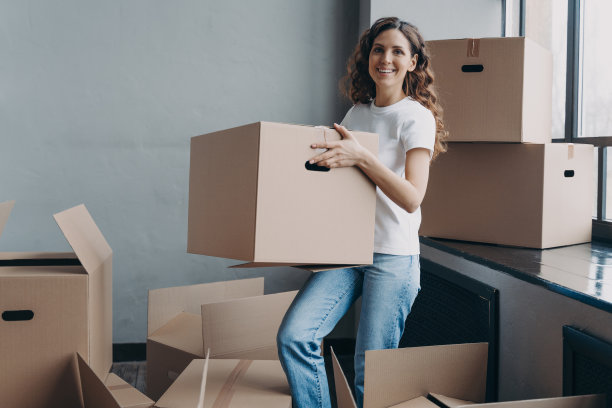 穿着牛仔裤和白色t恤的女孩拿着一个纸箱。快乐的女人打包东西搬家。图片下载