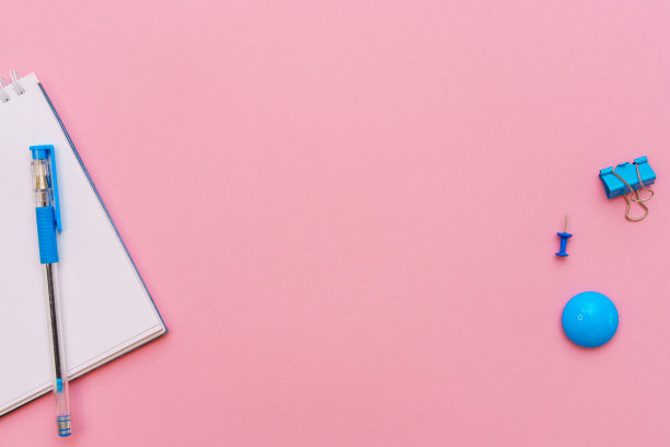 粉红色背景打开螺旋记事本，记事本和蓝色钢笔平躺在纸上图片下载