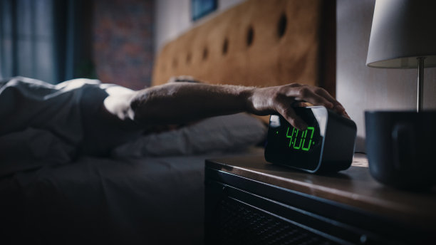 男人醒来，关掉闹钟。早起的富有成效的人准备开始充满新冒险的一天。床头床头柜的焦点是四点钟的时钟。卧室的公寓图片下载